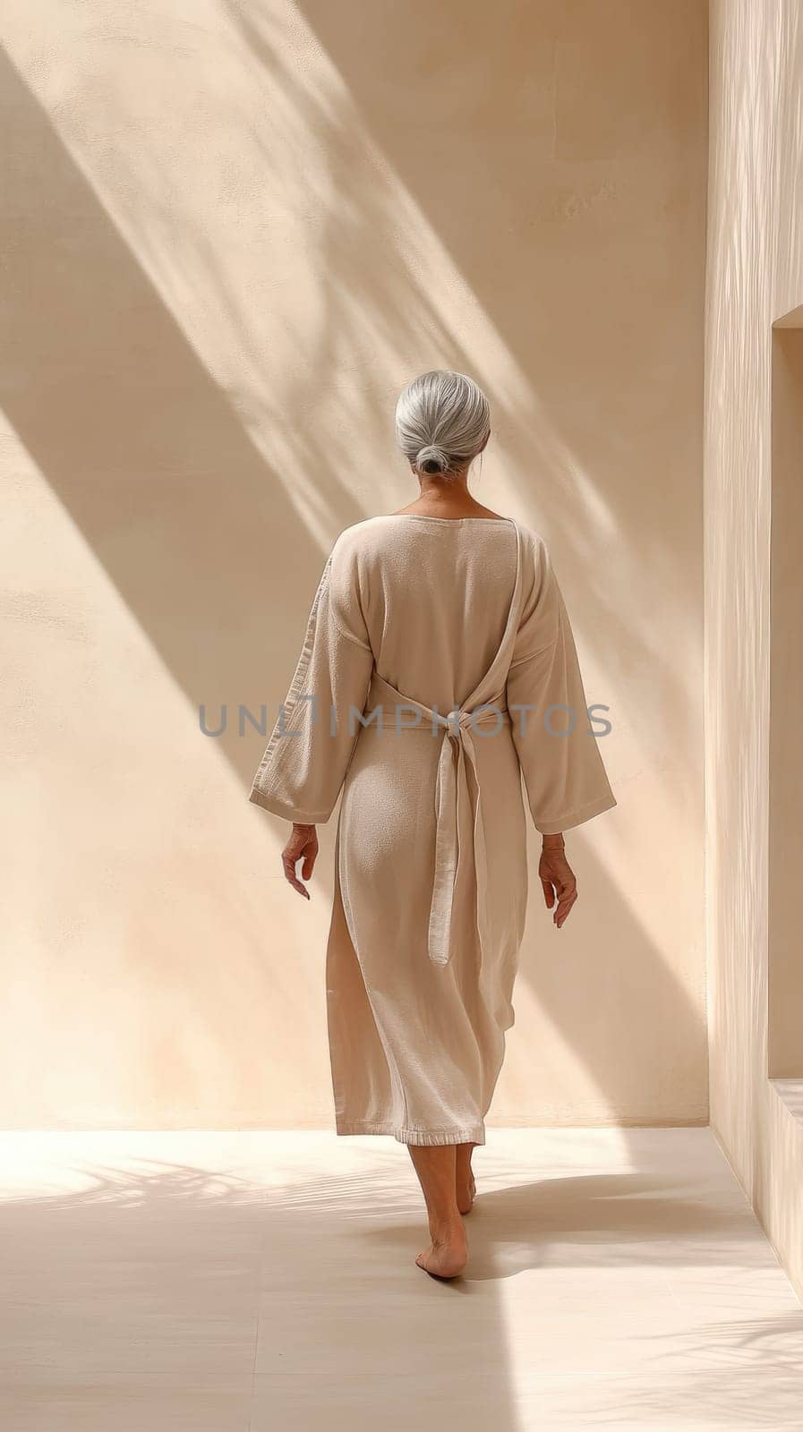 A senior silver-haired woman moves gracefully through a softly lit spa hallway, her robe flowing gently as she brushes her hands against a textured wall. The ambiance is calm and inviting.