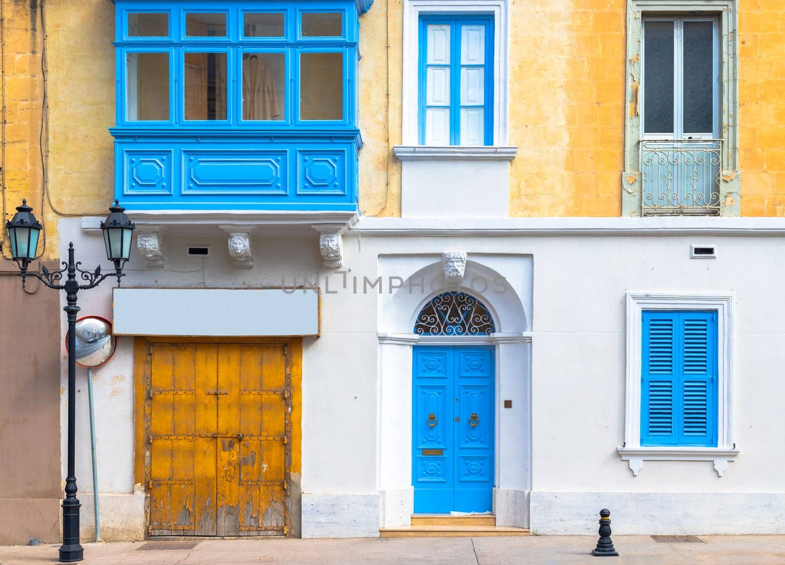 Facade of a traditional Maltese building with balcony, shuttered windows and garage gate.