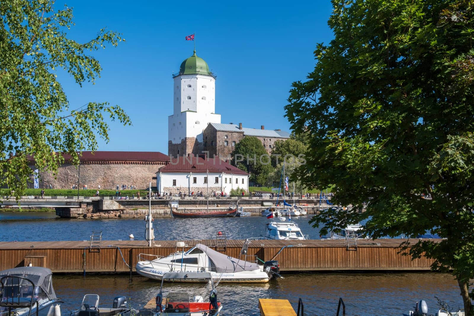 Vyborg, Leningrad region, Russia - 08.25.2024. A picturesque view of a historic Vyborg fortress with a green dome by a river and boats in the foreground.