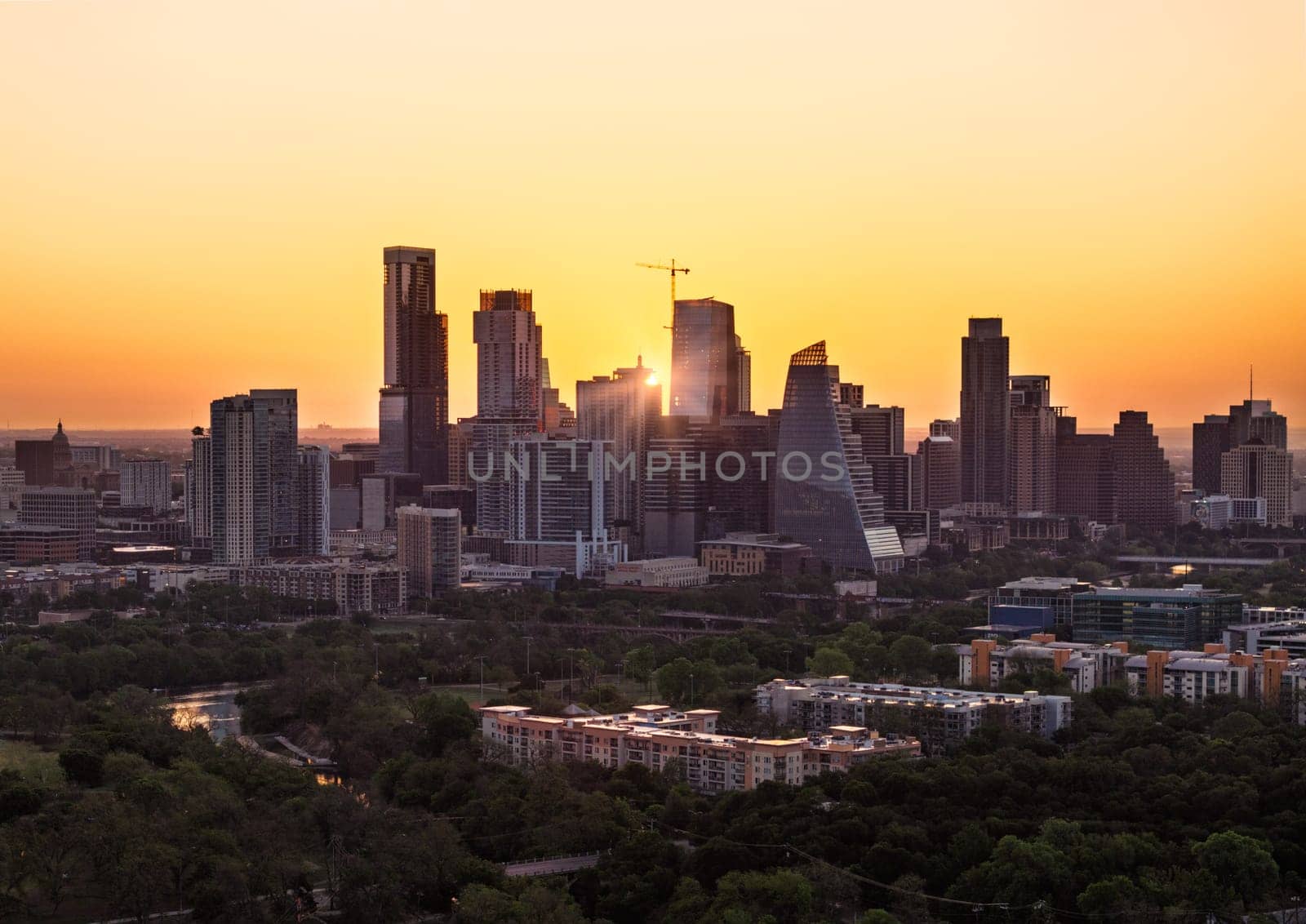 Rising sun appears between the skyscrapers of Austin, Texas at dawn in aerial view from Zilker park