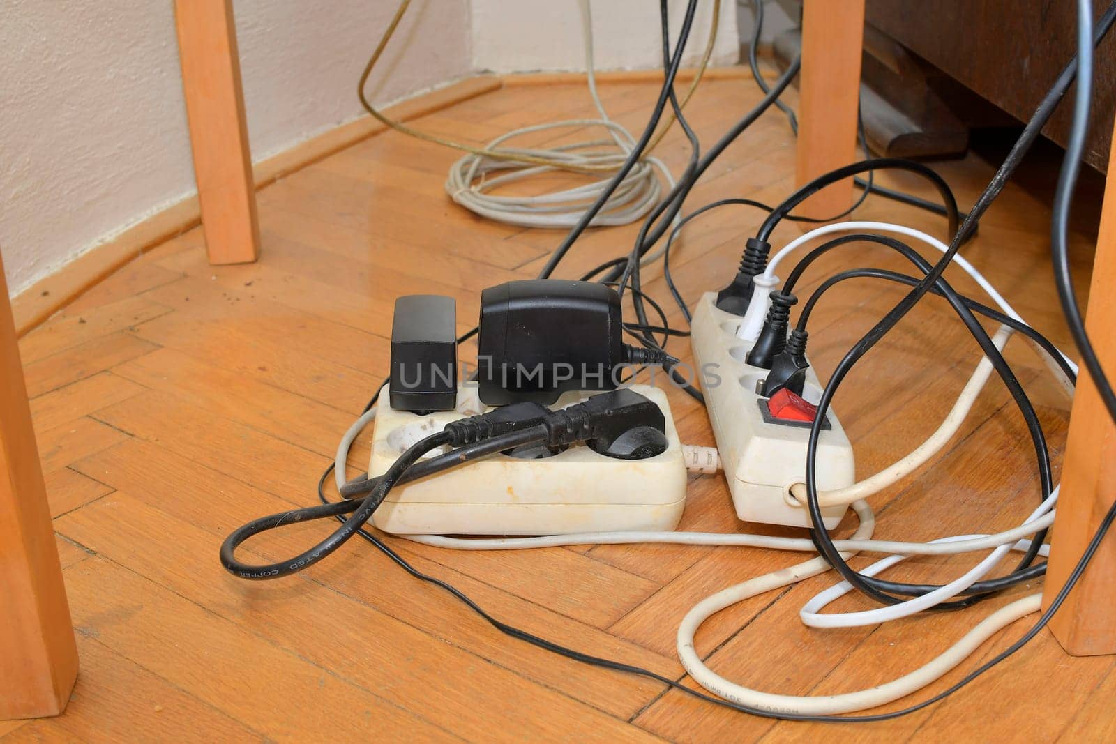 Cable chaos clutter from multiple electric wire extension cords and multi-contact plugs on wooden floor. Tangled cables on the parquet floor