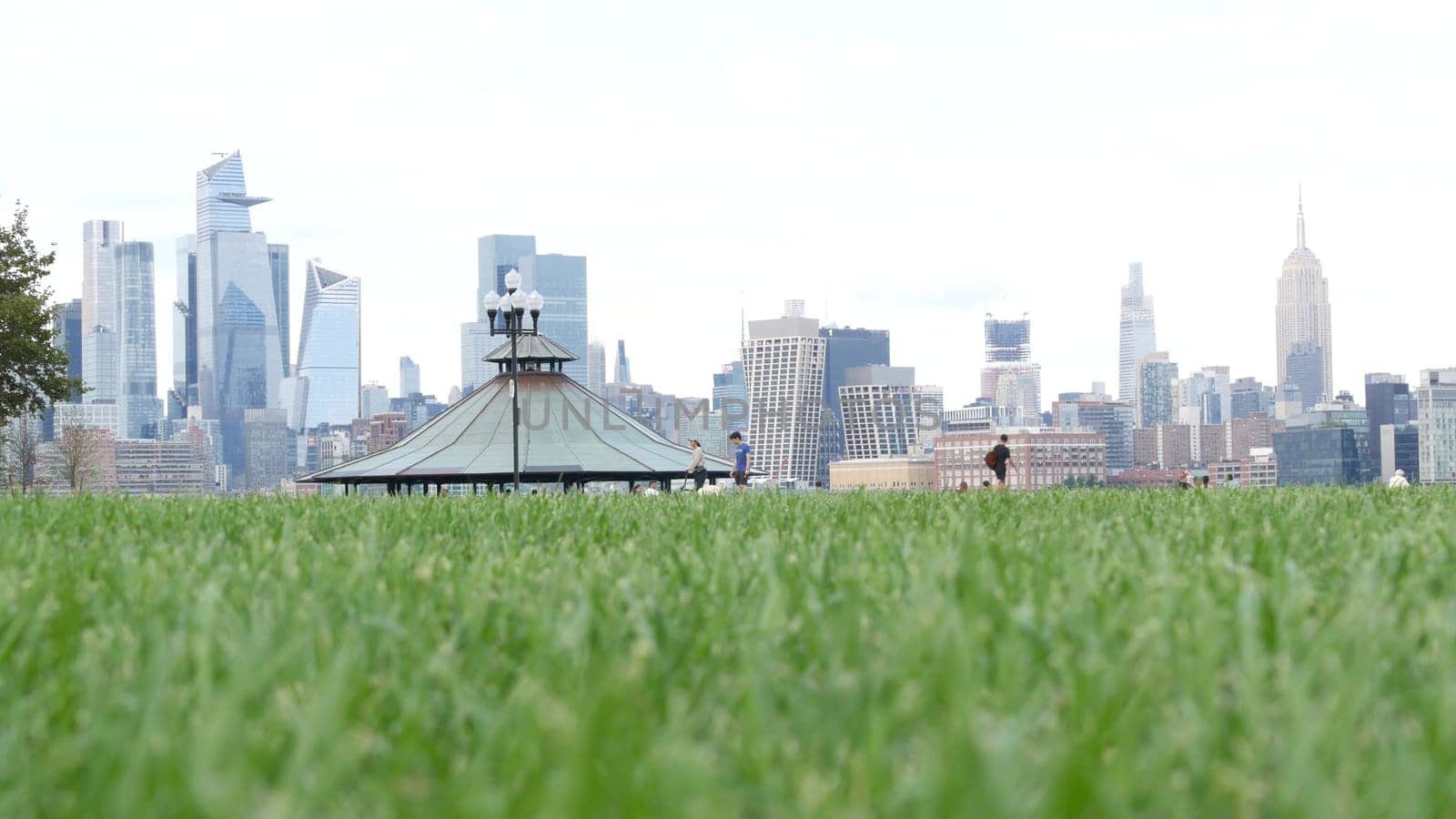 New York City, United States - 11 Sept 2023: Waterfront skyline, Manhattan Midtown Hudson Yards, riverfront skyscrapers. Waterside cityscape from Pier A Park, Hoboken, New Jersey. People on grass lawn