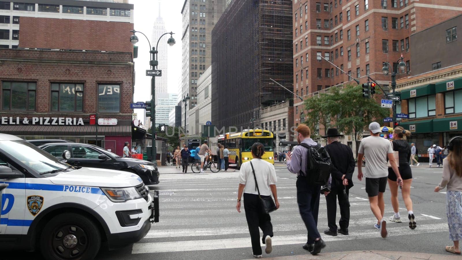 New York City, United States - 29 Aug 2023: Police patrol car, USA NYPD 911, Manhattan Midtown 34th street. American cop auto, 9 avenue. Urban road traffic. People, Empire State Building, yellow taxi.