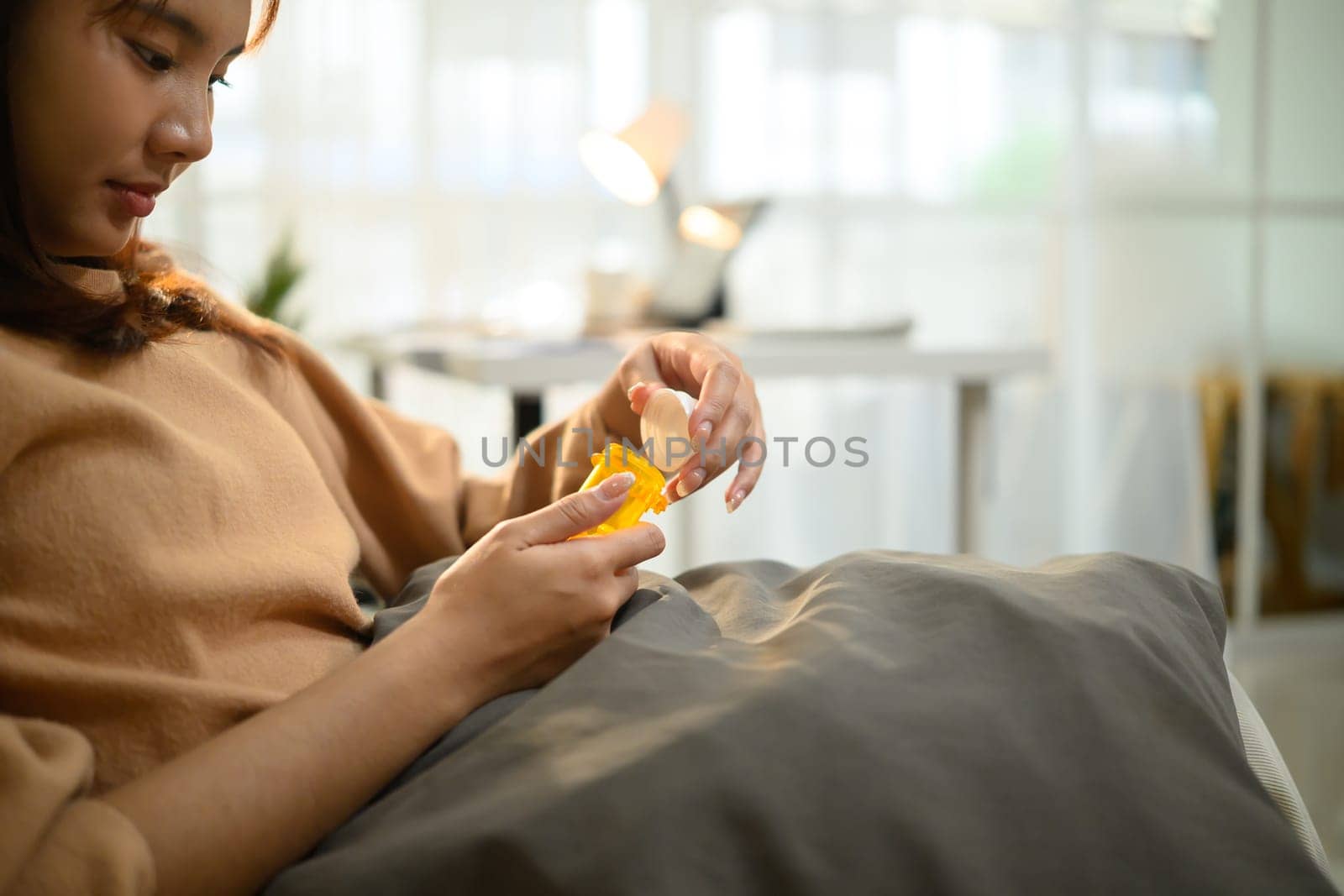 Young asian woman in casual clothes taking medicine while resting in a couch.