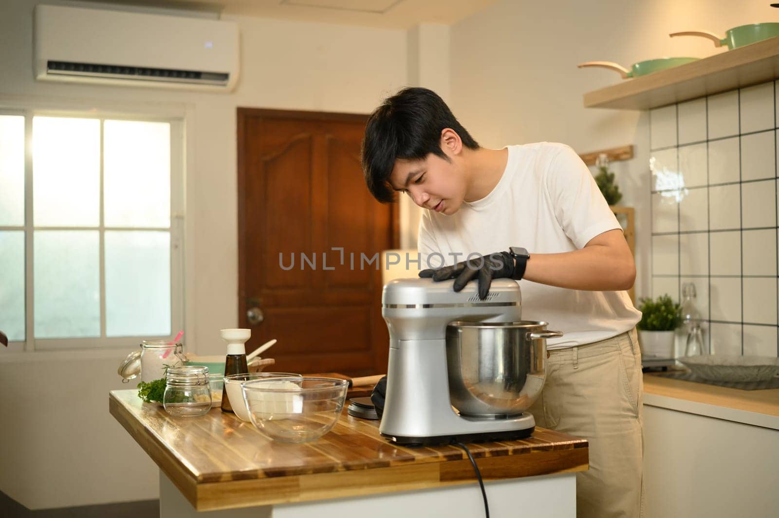 Young asian man preparing whipped cream with a stand mixer in home kitchen.