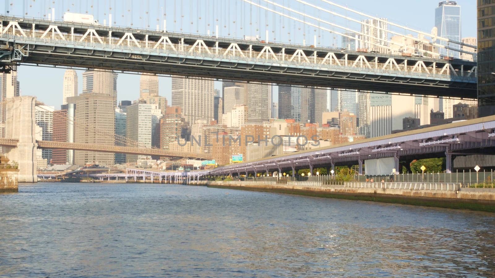 New York City, United States - 7 Sept 2023: Manhattan Bridge to Brooklyn. Waterfront downtown skyline cityscape, financial district skyscrapers from riverfront Pier 35. East river morning sunset.
