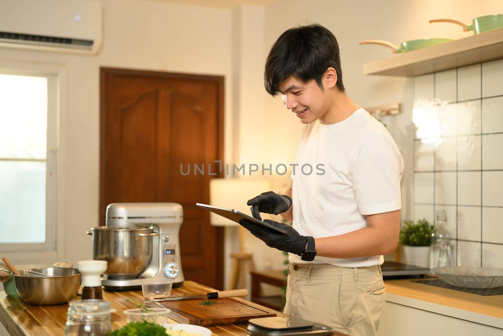 Asian man in kitchen checking a recipe on digital tablet while preparing whipped cream.