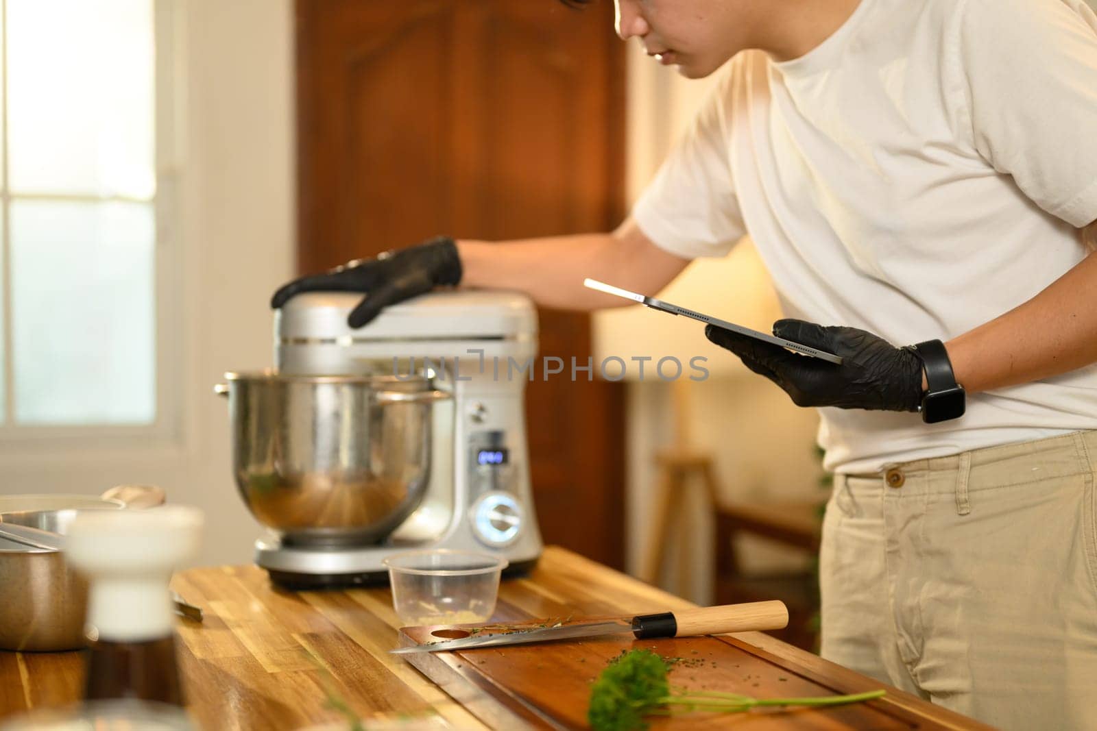 Asian man in kitchen checking a recipe on digital tablet while preparing whipped cream.