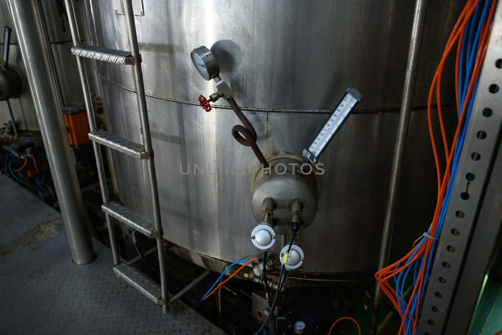 Stainless steel industrial tank with temperature and pressure gauges in a food processing facility.