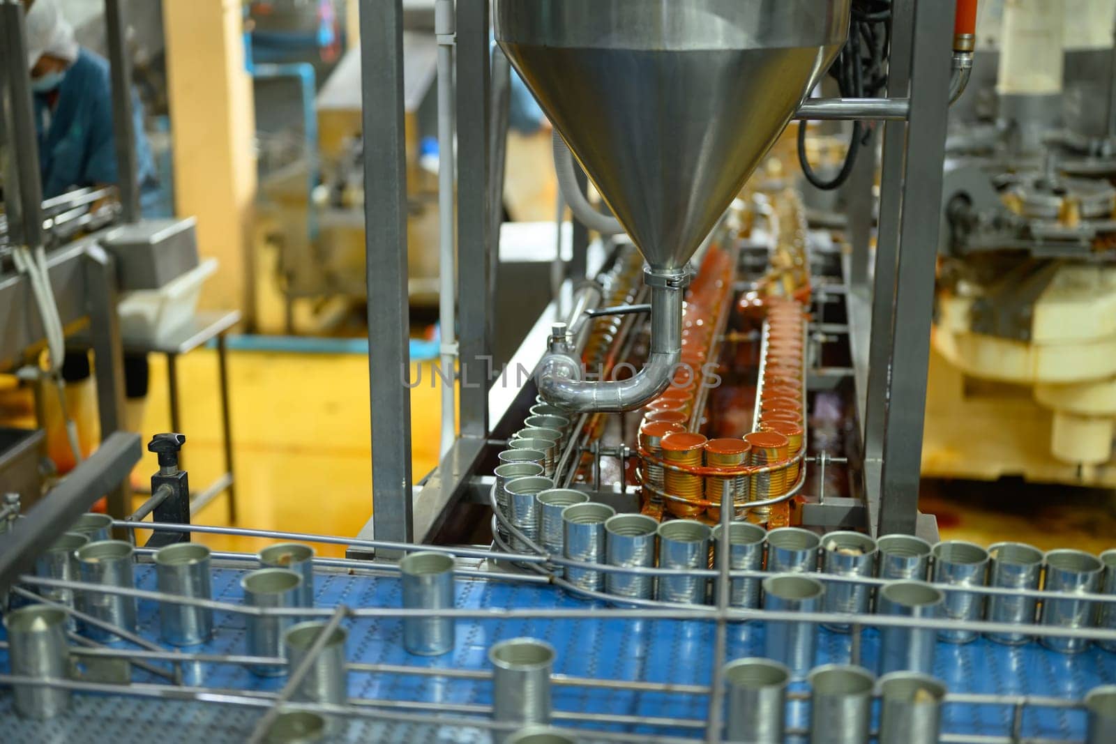 Automated factory line filling metal cans with food product in an industrial processing plant.
