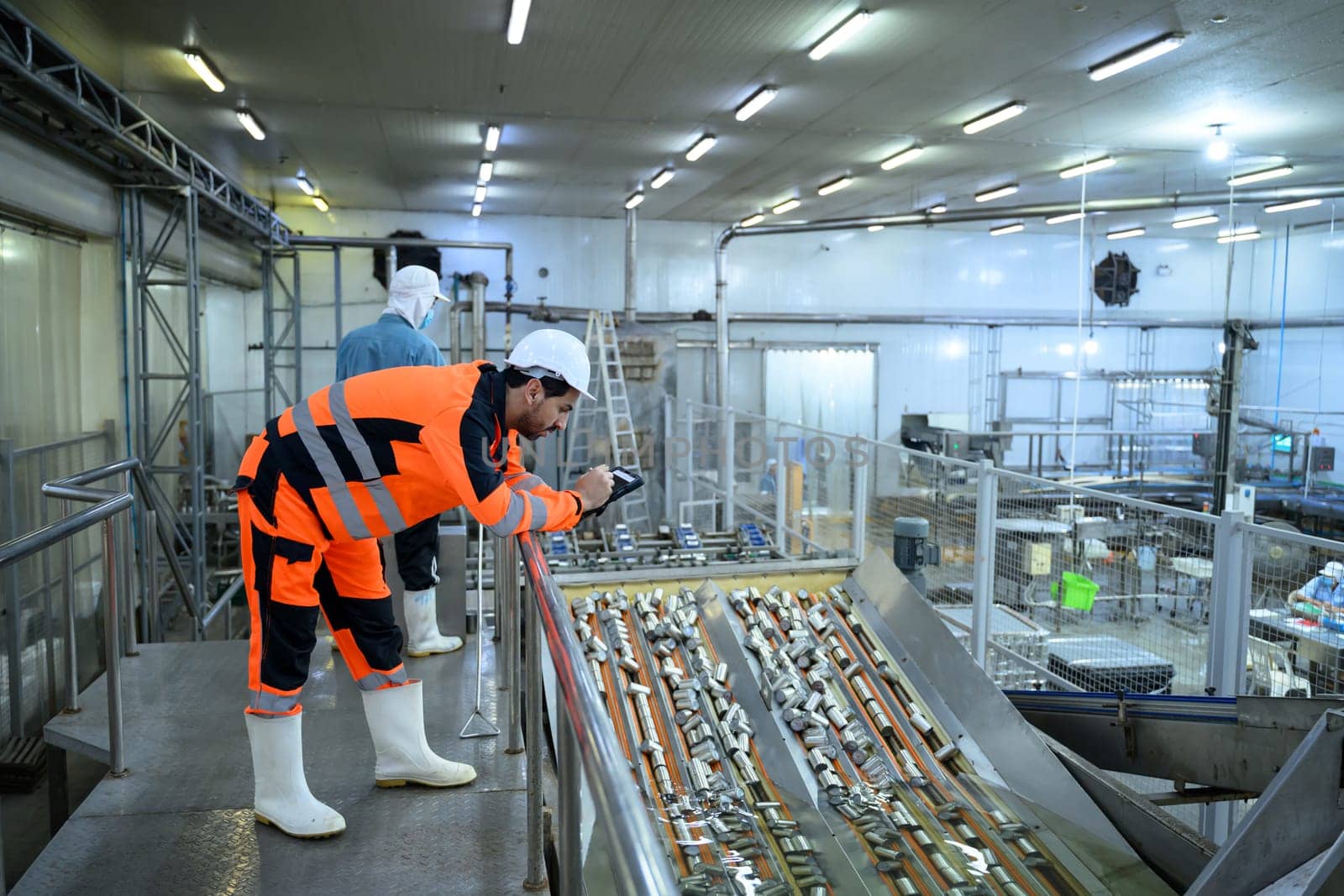 Factory inspector monitoring canned goods moving on a conveyor line in a food processing plant.