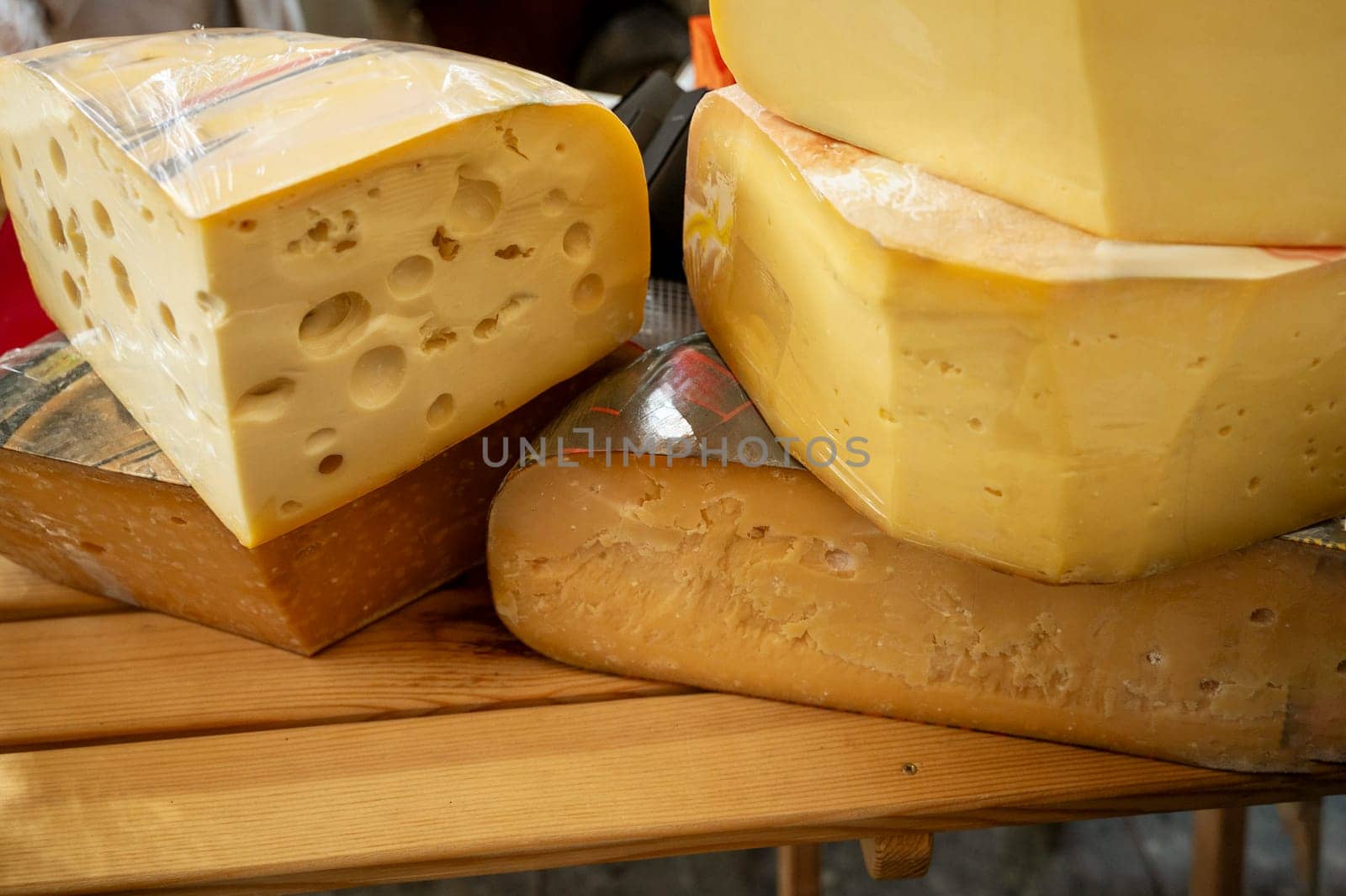 large circles of fresh cheese in section. Various types of cheese displayed at a market stall. Cheese blocks and slices arranged for sale at a farmers market. High quality photo