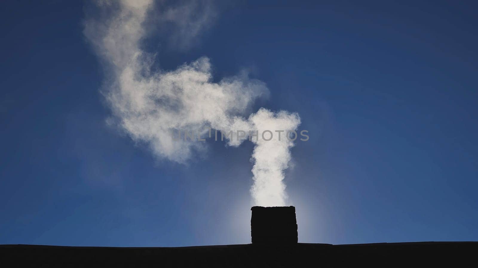 White smoke billowing from a chimney against a bright blue sky on a sunny day, creating a striking contrast with the surrounding atmosphere