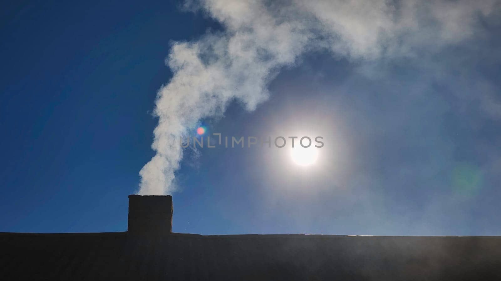 White smoke rising from a chimney on a sunny day, set against a backdrop of a clear blue sky, creates a cozy and inviting atmosphere