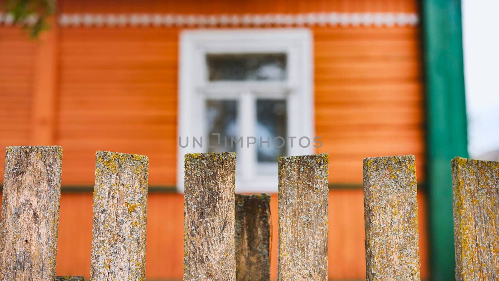 Weathered wooden fence bordering orange farmhouse, white window framing rustic countryside charm and nostalgic rural setting