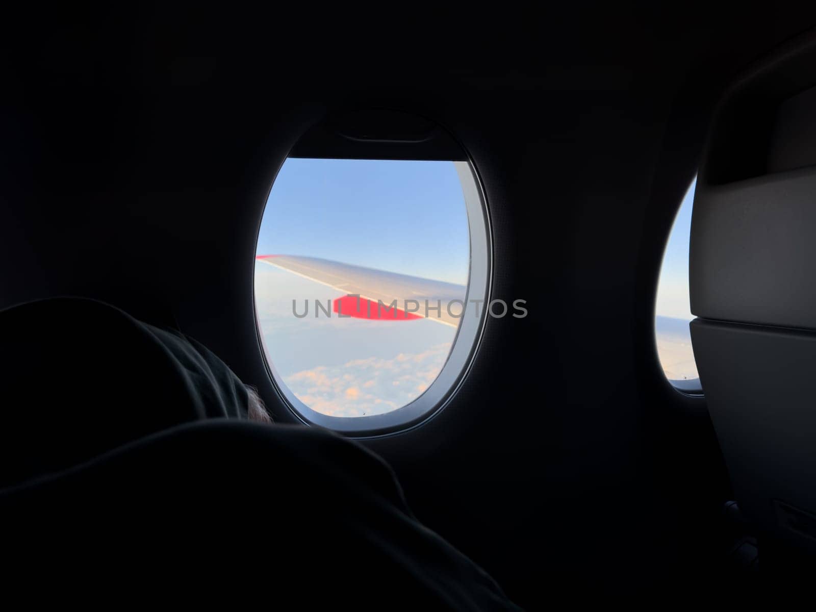 Peaceful moment inside airplane cabin with sleeping passenger near window, soft light illuminating clouds and wing outside, capturing calm travel and quiet relaxation at high altitude