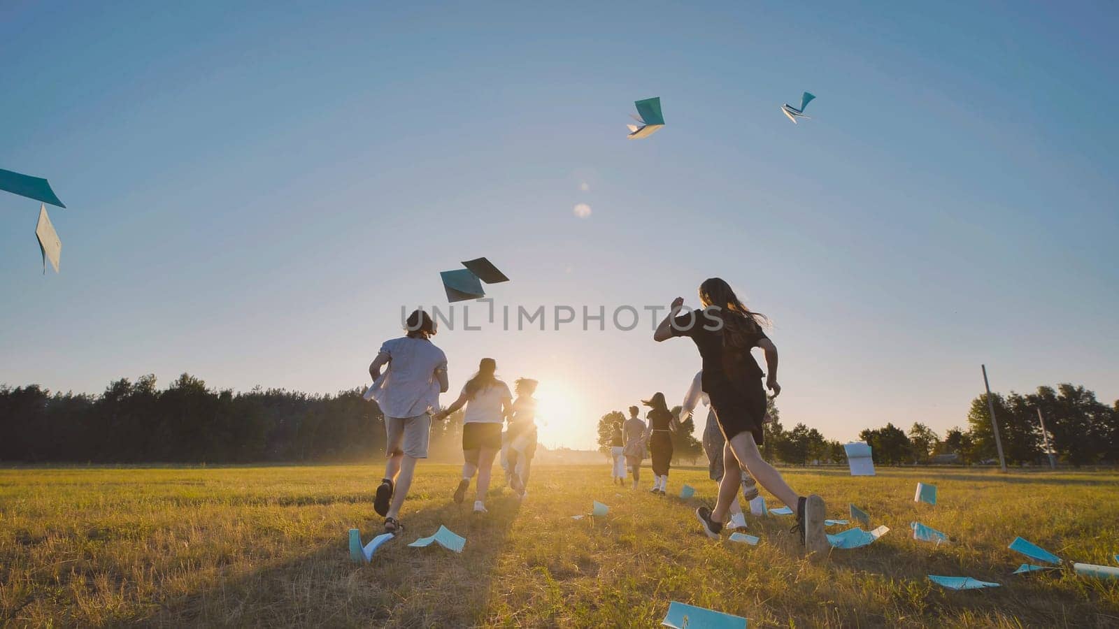 High school students rejoice in the end of the school year by sprinting through a field at sunset and tossing their notebooks into the air