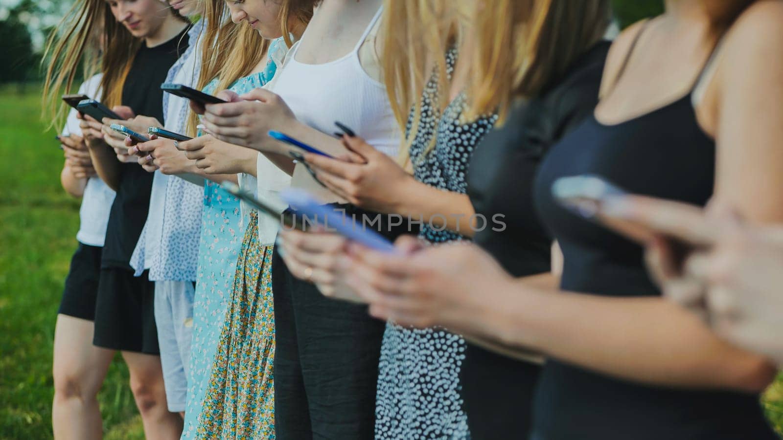 Group of high school students enjoying summer outdoors, engaging with smartphones while connecting with friends and sharing experiences