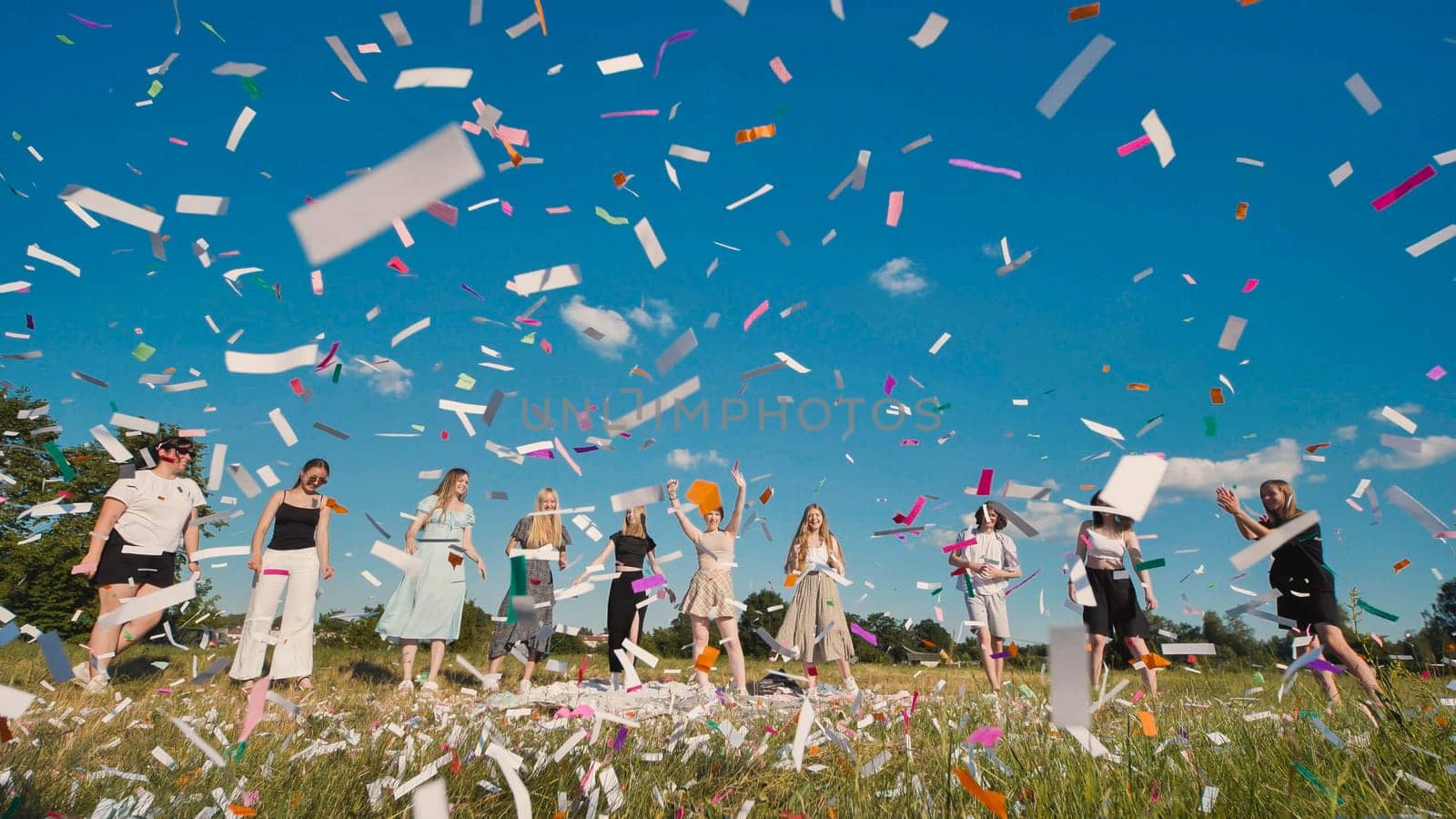 Group of cheerful high school students throwing colorful confetti in the air, celebrating their graduation in a sunny field