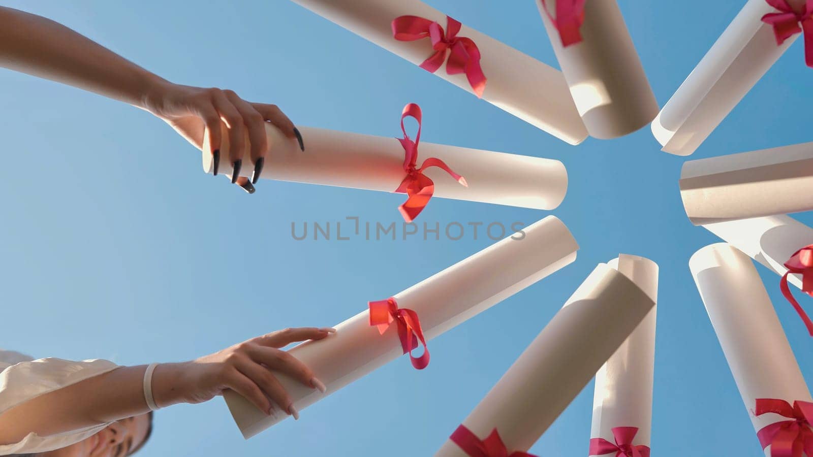 Graduates gathered in a circle, proudly displaying diplomas against a clear blue sky to celebrate their academic success and completion of studies