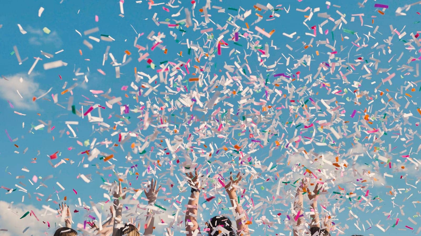 Group of cheerful students throwing colorful confetti in the air celebrating graduation day under a beautiful blue sky