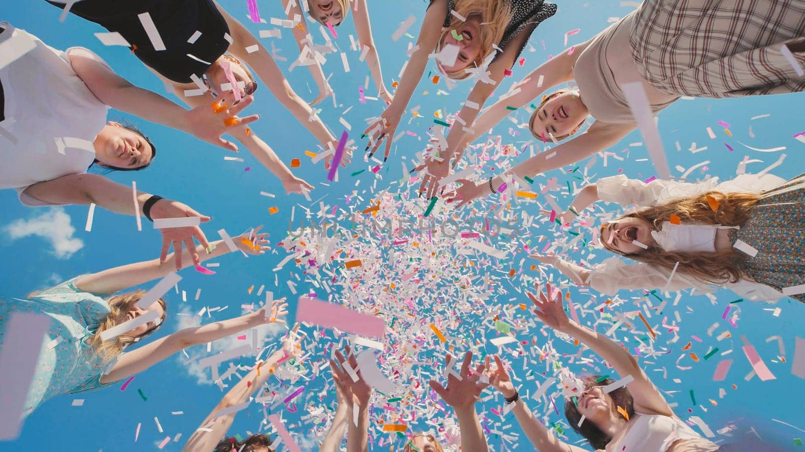 Group of cheerful high school students throwing colorful confetti in the air, celebrating graduation during summer