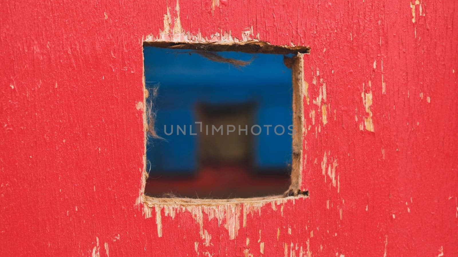 Square hole revealing blurred blue background in red painted wood