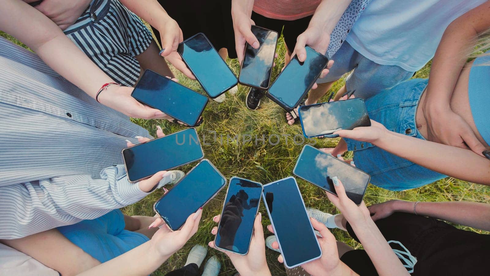 Students gathered in a circle on the grass, holding smartphones with blank screens, exchanging digital content and memories