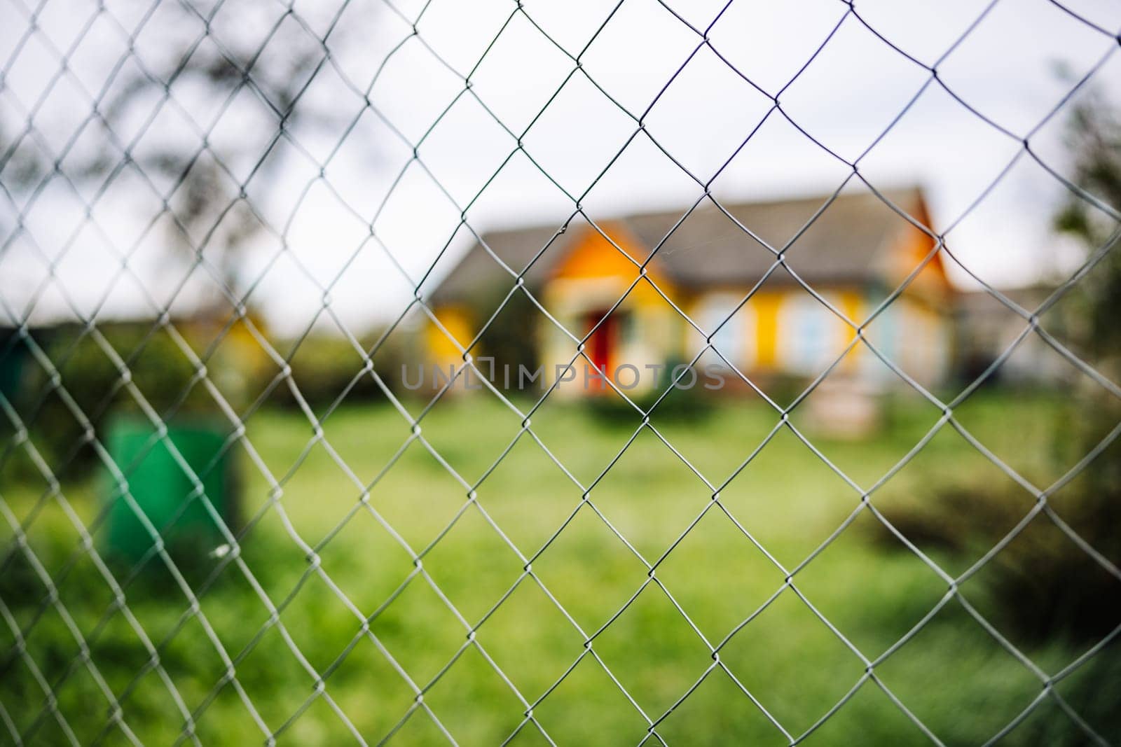 Chain link fence is blocking access to colorful house with green lawn