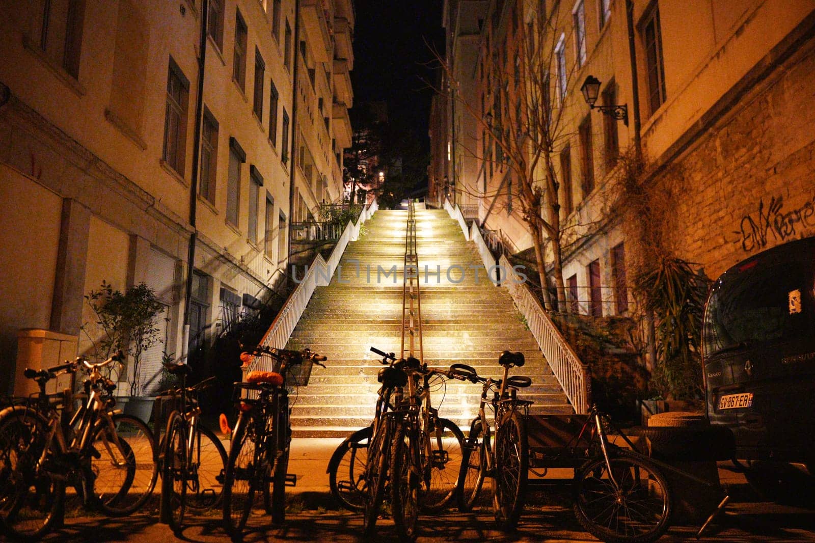 Wide urban staircase lit at night between residential buildings, with multiple bicycles parked at the base and warm lighting ambiance.
