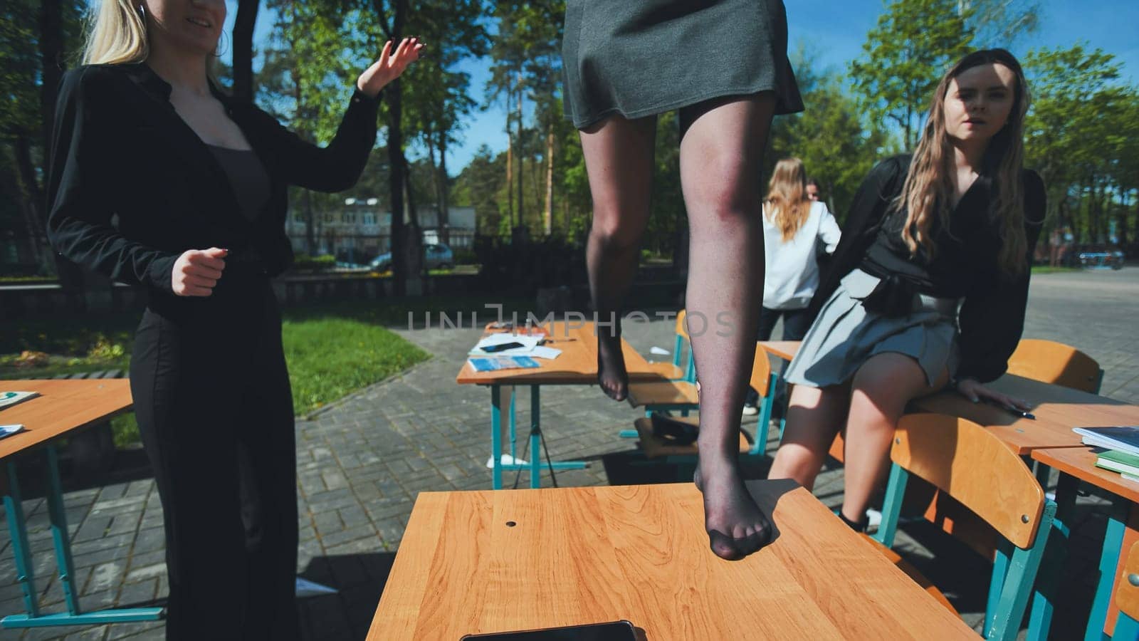 Schoolgirls are enjoying their break time, jumping on desks in the schoolyard, expressing youthful exuberance and camaraderie