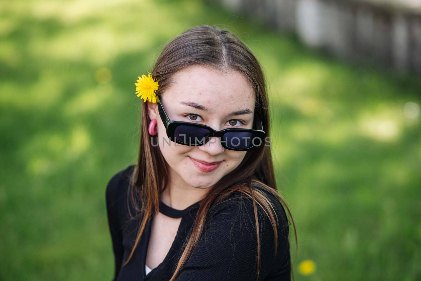 Portrait of a smiling female high school student with a dandelion behind her ear and sunglasses, enjoying a break during the school day
