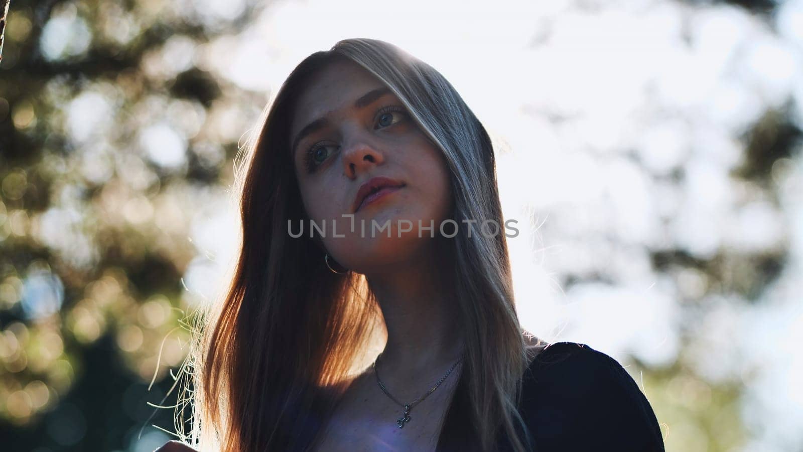 Portrait of a thoughtful teenage student with long hair, illuminated by sunlight filtering through trees, evoking contemplation and aspirations