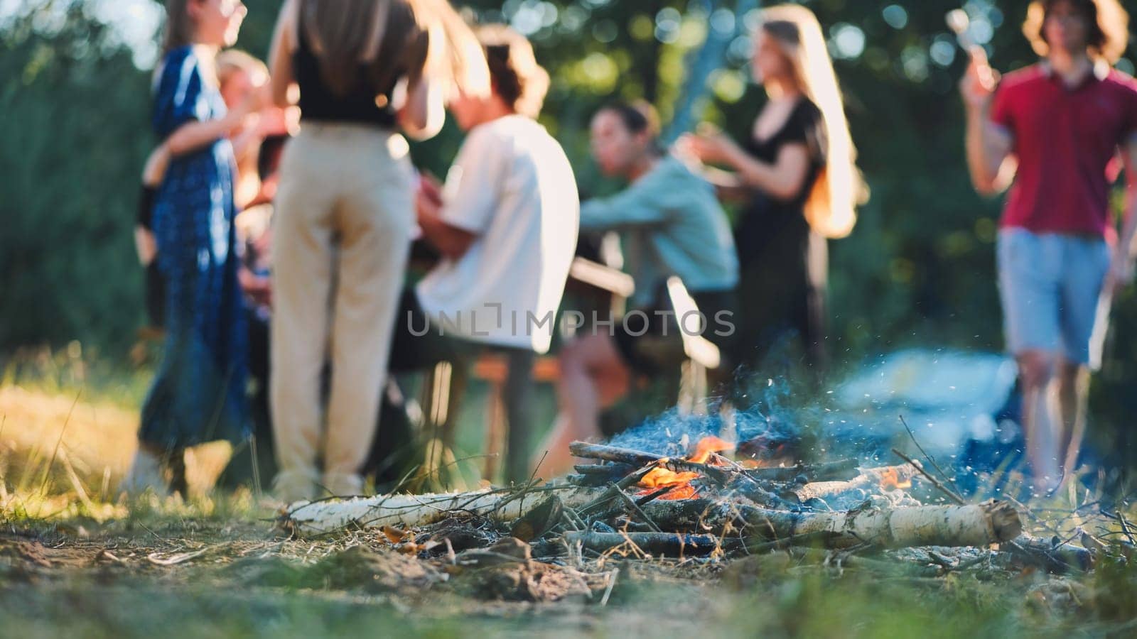 Group of students celebrating their graduation, gathered around a lively bonfire in a serene natural setting, enjoying friendship and joy