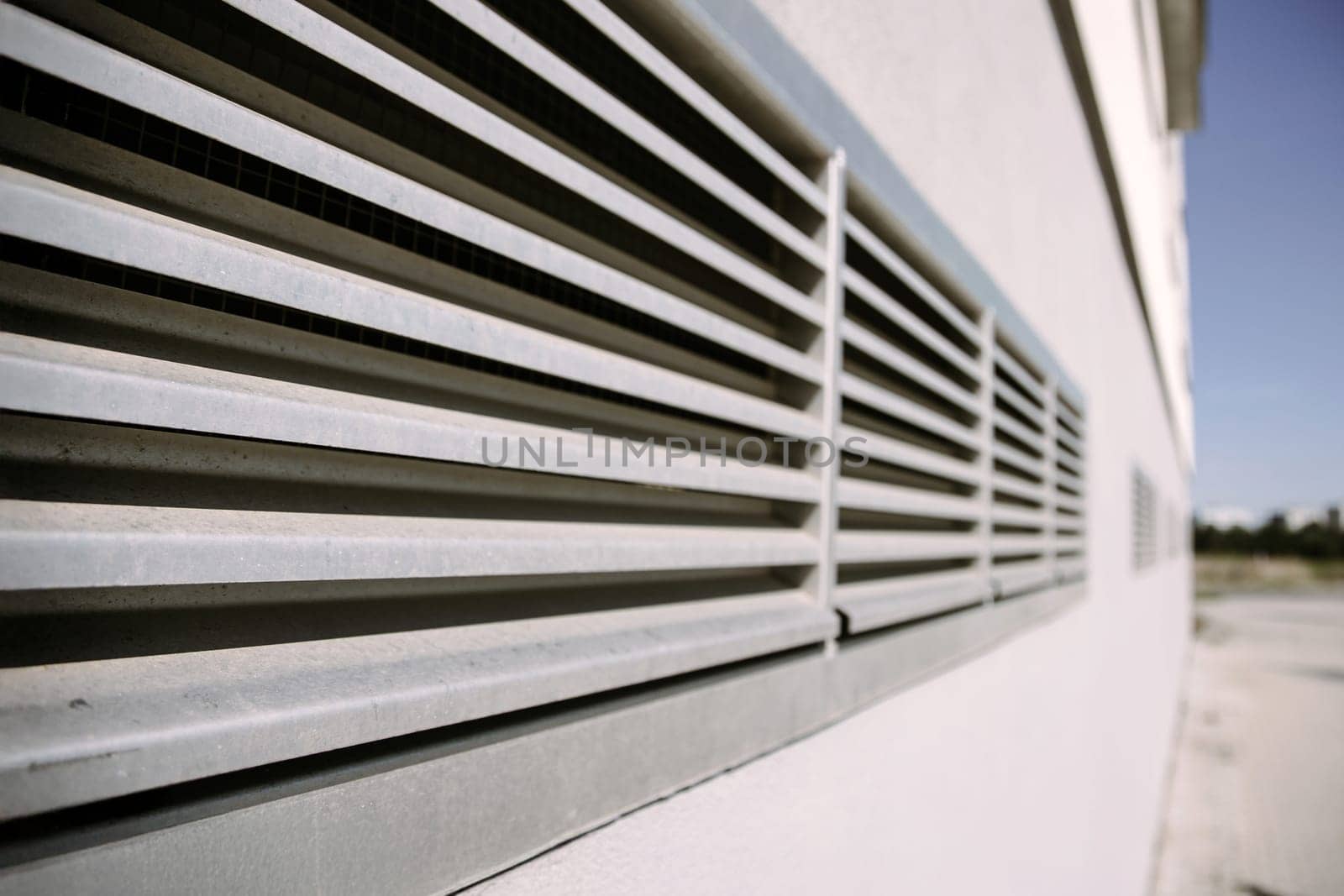 A metal ventilation grille mounted on the wall of a modern industrial building. Great for illustrating concepts of airflow, HVAC systems, construction, and urban infrastructure