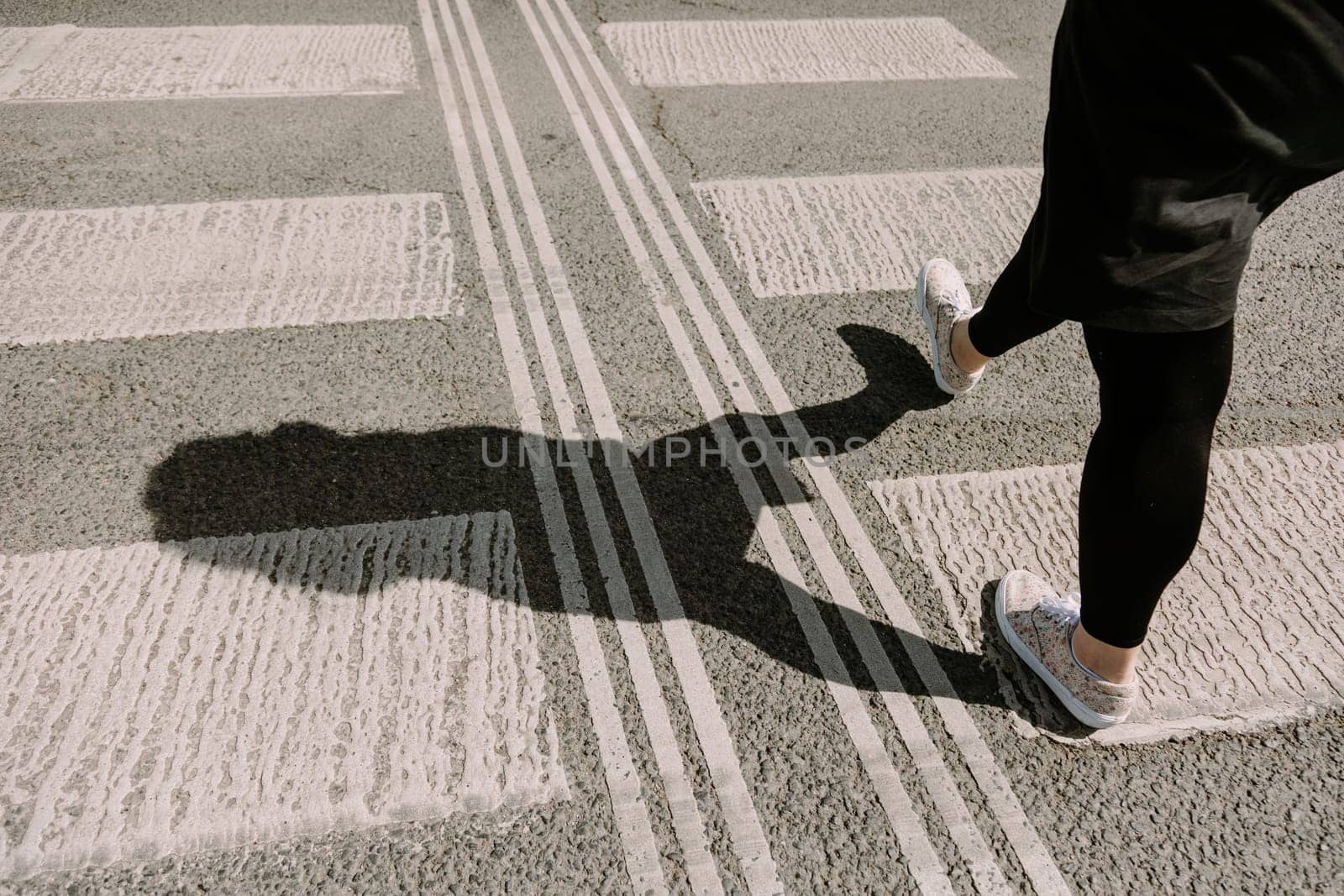 Woman walking across a pedestrian crosswalk with a clear shadow cast on the pavement. Perfect for themes of city life, independence, movement, and everyday moments in urban environments