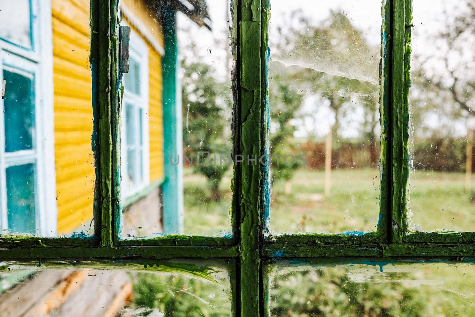 Dirty window glass with peeling paint showing a colorful house and garden