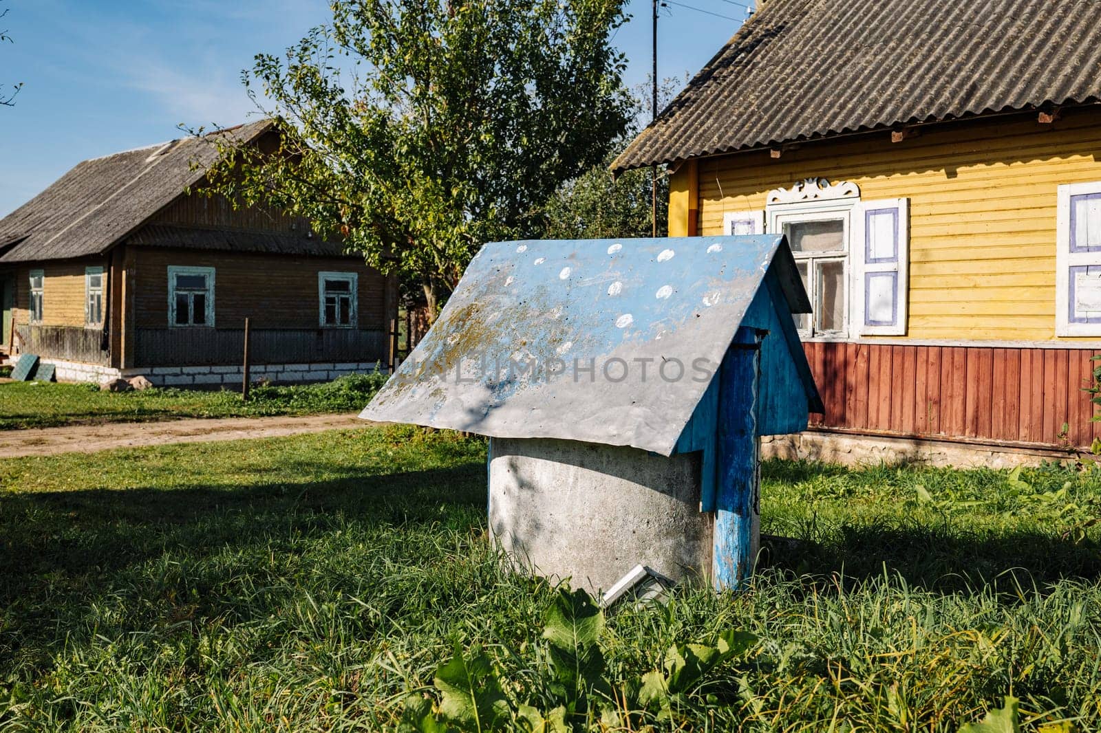Old aged water well with aged wooden roof and wooden houses in countryside