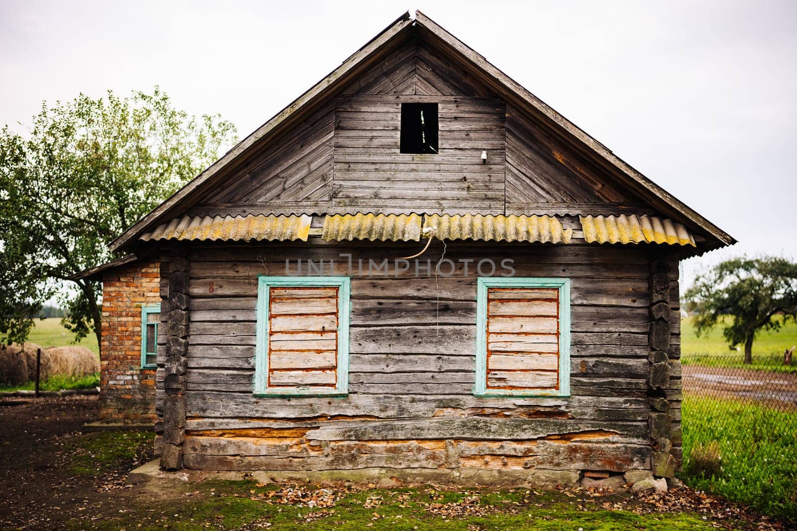 Weathered wooden facade of an old abandoned house with broken windows in a rural landscape