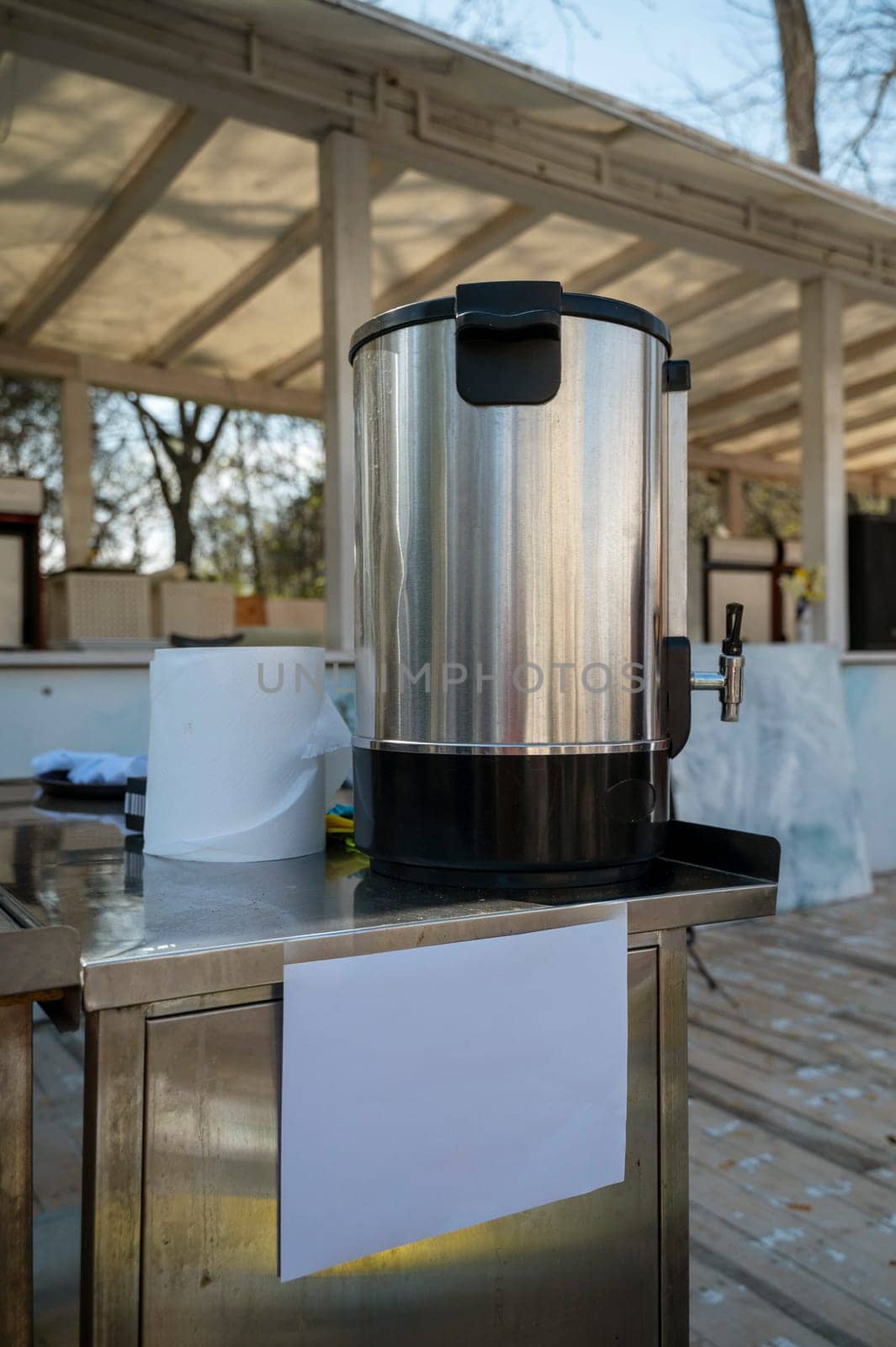 Large stainless steel container for hot water or mulled wine. City food fair in the open air. Paper towels nearby.