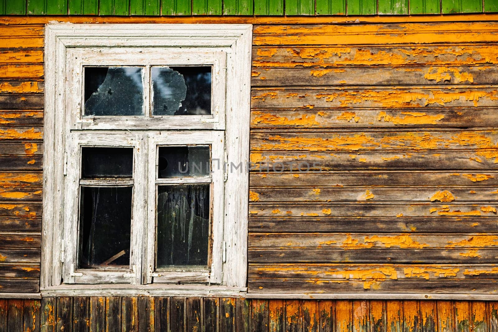 Weathered window with broken glass and peeling orange paint on a wooden facade, showing decay and neglect