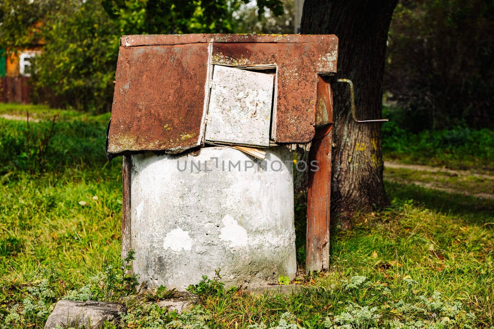 Rusty abandoned water well slowly decaying in the summer countryside near a tree