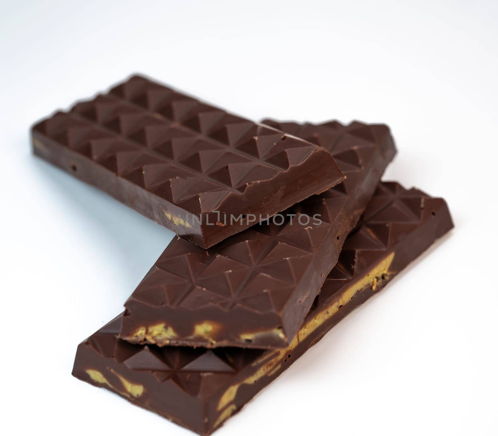 Stacked layers of kadaif embrace a generous coating of rich chocolate and are topped with a pistachio, showcasing the delightful texture and flavors in a culinary presentation.