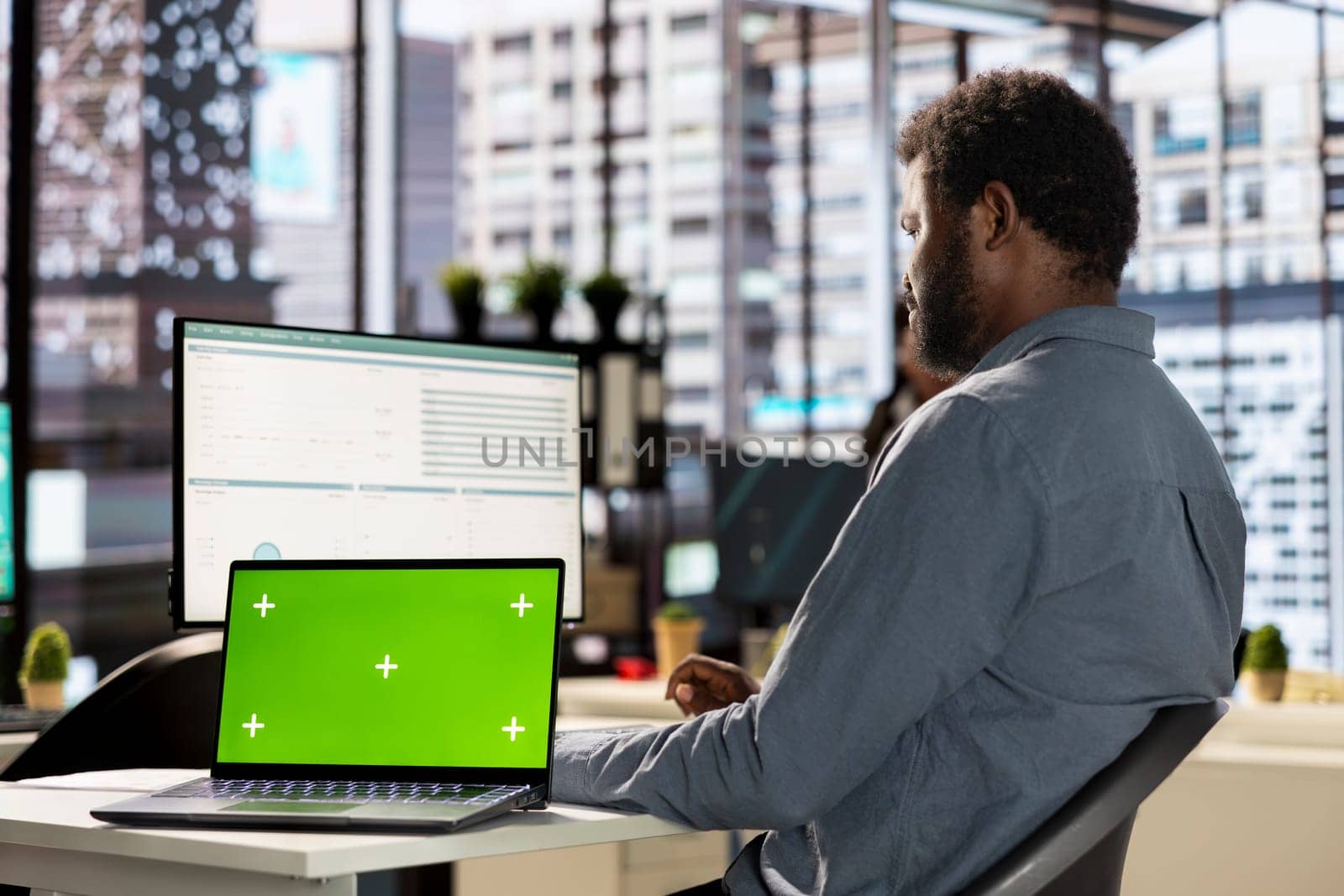 Male business manager at desk looking at mockup screen and solving tasks for company objectives accomplishment. Fighting for performance goals to ensure successful corporate outcomes.