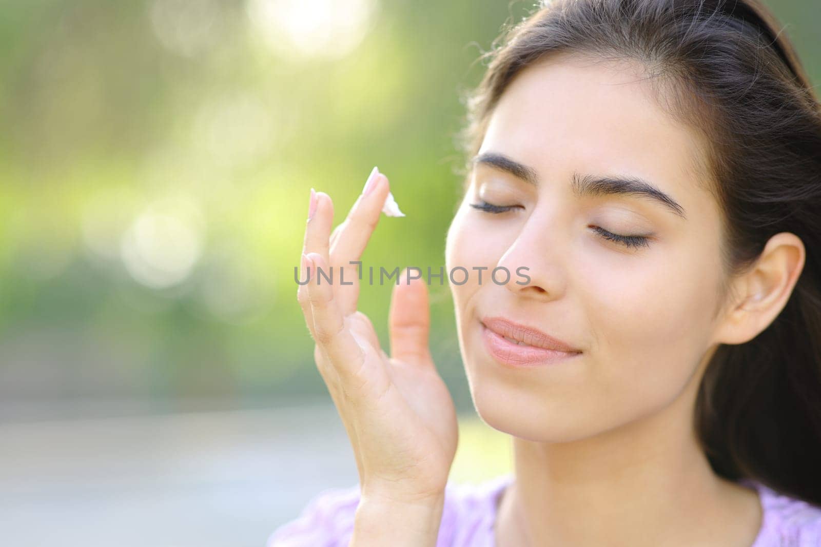 Beautiful woman hydrating face skin with cream in a park