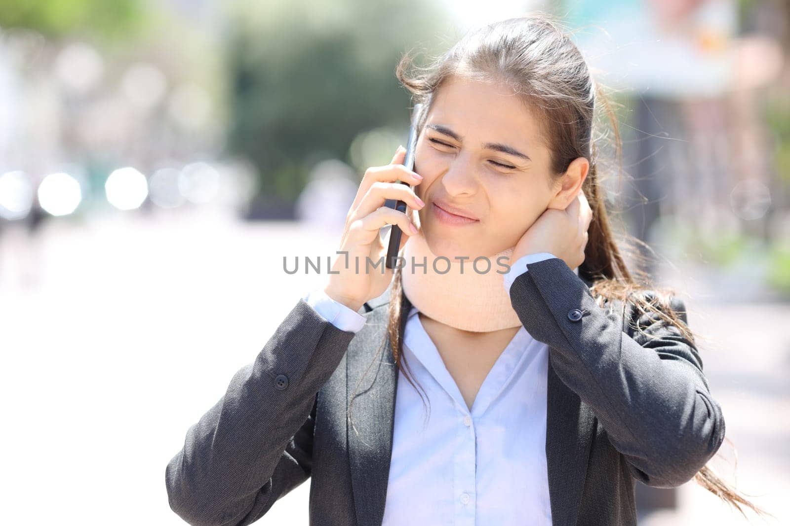 Convalescent executive wearing neck brace calling doctor on phone in the street