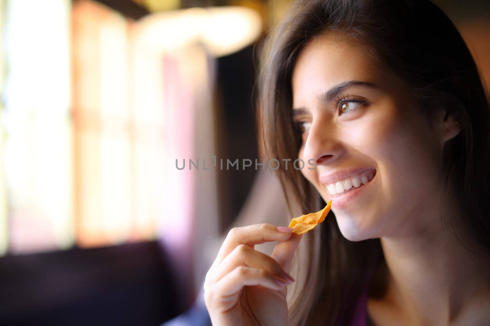 Happy restaurant customer eating chips looks at side through a window