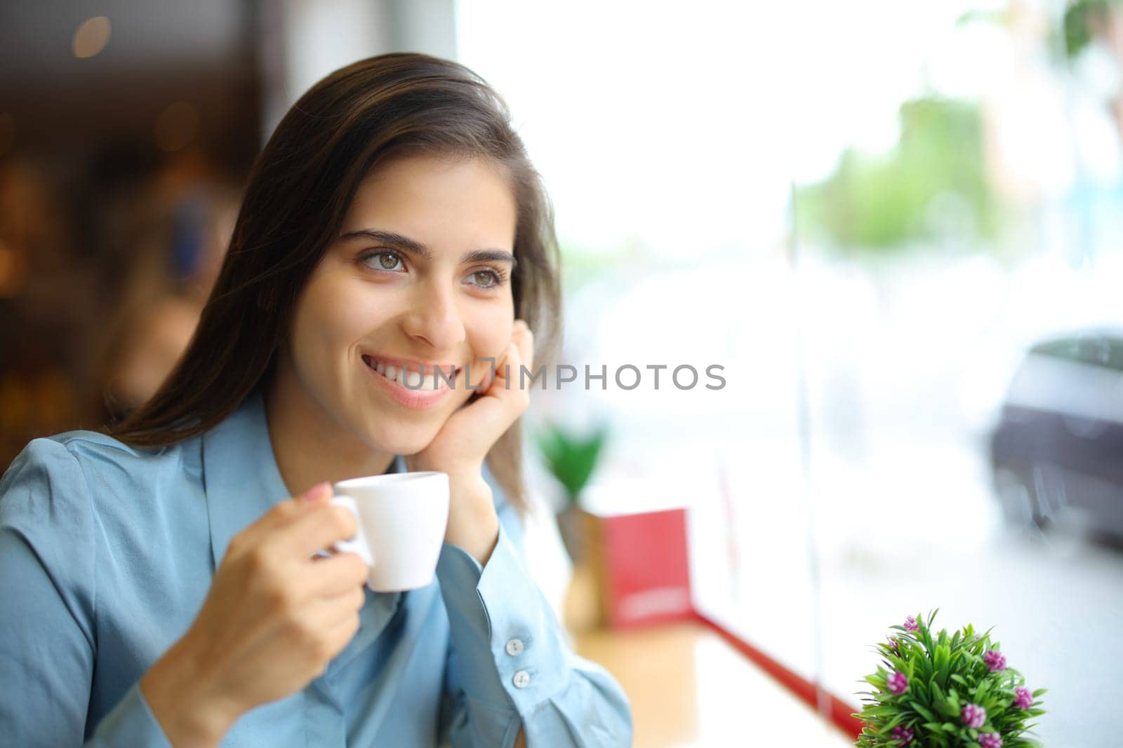 Happy woman drinking coffee in a bar looking away through a window