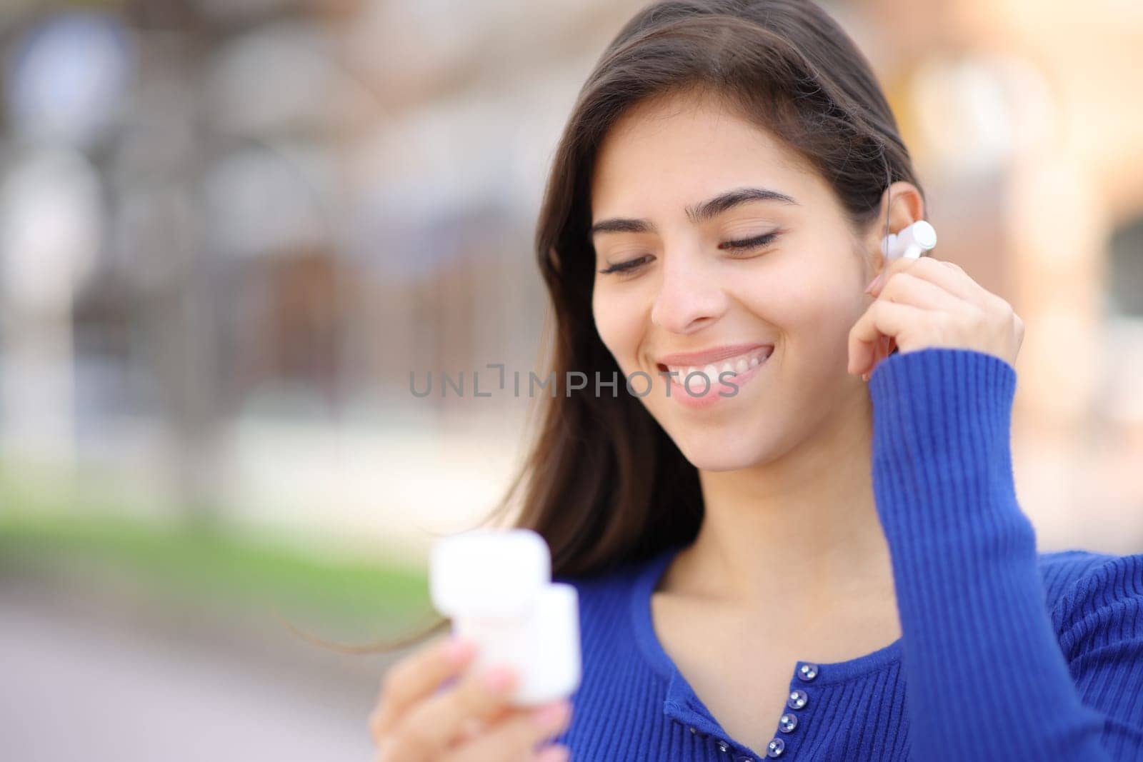 Happy woman putting wireless earbud on ear in the street