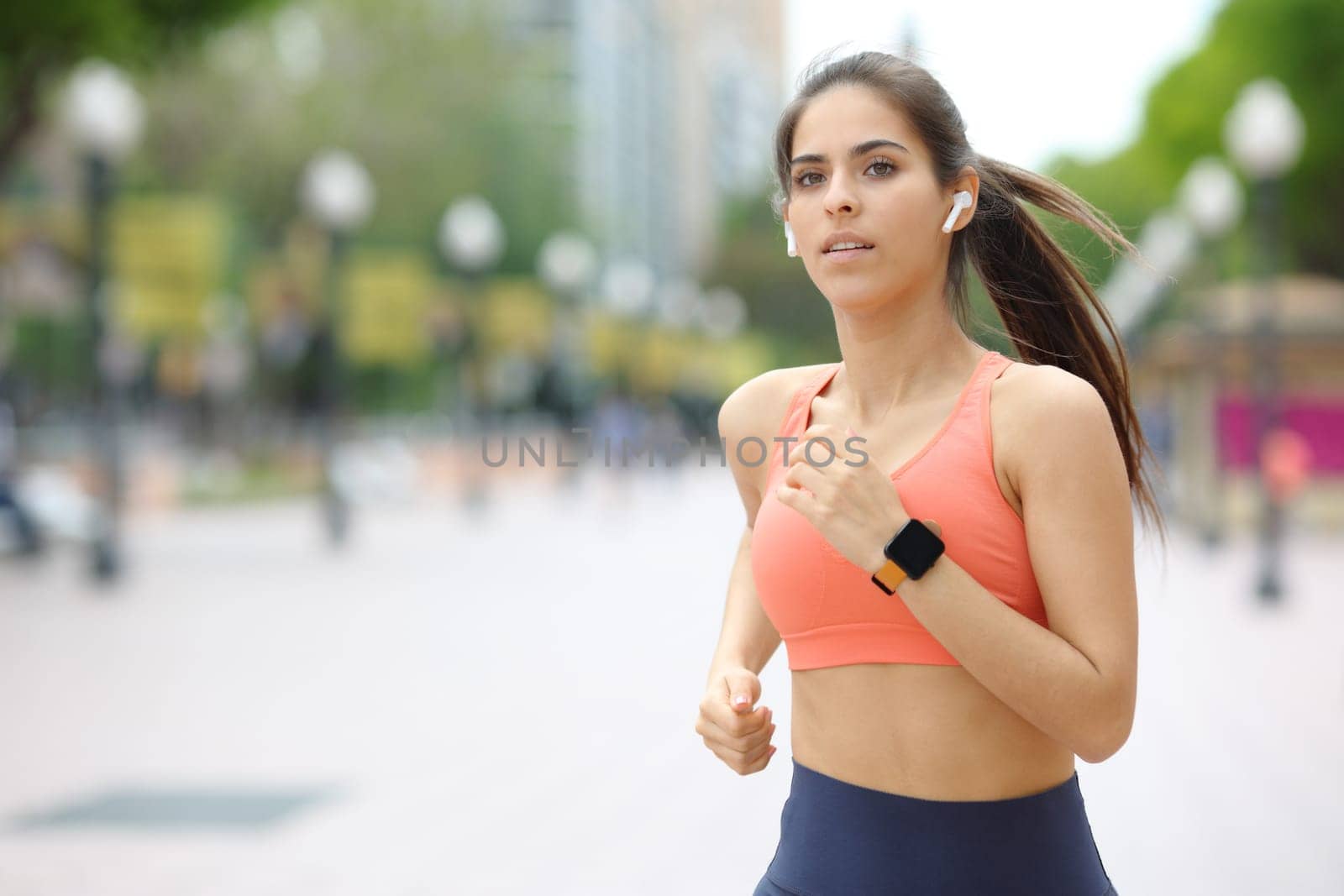 Runner running wearing earbud and smartwatch listening to music in the street